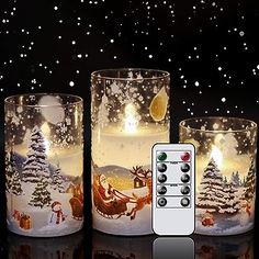 three lit candles with christmas scenes on them and a remote control in the foreground