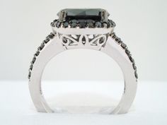 an engagement ring with black and white diamonds on the sides, set in 18k white gold