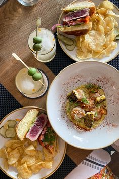 three plates with food on them sitting on a table next to chips and olives