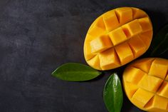 two pieces of mango sitting next to each other on top of a black surface with green leaves