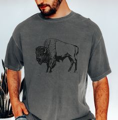 Bison Tee Shirt, Mens Buffalo Tshirt The Comfort Colors C1717 100% Ring Spun Cotton T-Shirt is very appropriately-named. All colors are inspired by nature and have a perfect lived-in, weathered look. Shirts are sent through a unique dyeing process that makes them incredibly soft and long-lasting. Each piece is soft-washed 50 times before making its way to you! Stitched at the collar, armhole, sleeves and bottom hem for ultimate durability, you will notice the density and quality of this shirt, b Casual Gray T-shirt For Outdoor, Rugged Relaxed Fit Outdoor Top, Rugged Relaxed Fit Top For Outdoor, Rugged Outdoor Relaxed Fit Top, Soft-washed Relaxed Fit T-shirt For Outdoor, Outdoor Soft-washed Short Sleeve T-shirt, Outdoor Graphic Tee Soft-washed, Perfect Live, Mens Tee Shirts