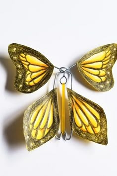 a yellow butterfly is attached to a metal hook on a white surface with the wings open