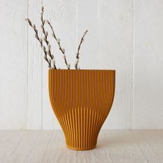 a yellow vase with branches in it on top of a wooden table next to a white wall