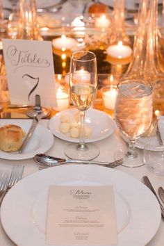 the table is set with white plates and silverware, candles, and menu cards