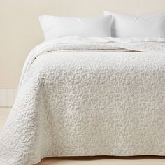 a white bedspread with two pillows and one pillow on the floor next to it