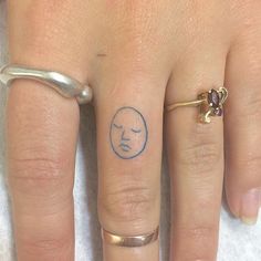 a woman's hand with two rings on it and a small face tattooed on the ring finger