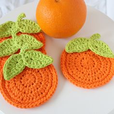 two crocheted oranges on a plate next to an orange with green leaves