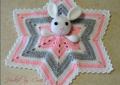 a crocheted blanket with a stuffed animal on it's back and pink, gray, white and grey colors