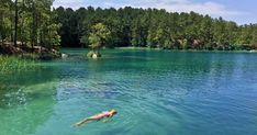 a man swimming in the middle of a lake surrounded by trees and water with people floating on it