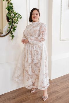 a woman standing in front of a mirror wearing a white lace dress with long sleeves