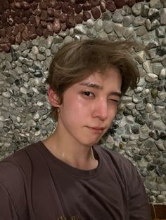 a young man sitting in front of a stone wall