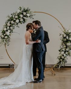 a bride and groom kissing in front of an arch decorated with white flowers at their wedding