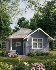 a small blue house in the middle of some grass and trees with flowers around it