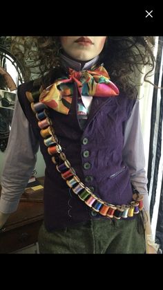 a man with long hair wearing a purple vest and colorful bow tie is standing in front of a mirror