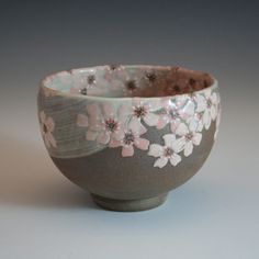 a gray and white bowl with pink flowers painted on the inside is sitting on a table