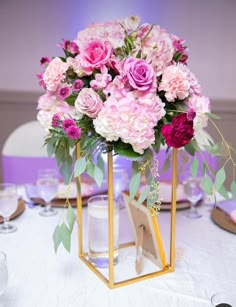 a vase filled with pink and purple flowers on top of a white table cloth covered table