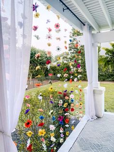 an outdoor area with flowers hanging from the ceiling and curtains on the side of it