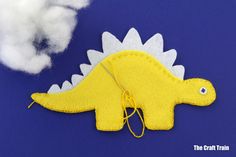 a yellow dinosaur brooch sitting on top of a blue surface next to white clouds