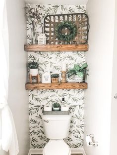 a bathroom with two shelves above the toilet and plants on the wall next to it