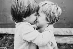 two small children are playing with each other in black and whit photo by the wall