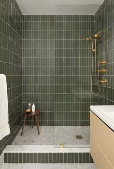 a green tiled bathroom with a wooden stool and shower head next to the bathtub