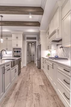 a large kitchen with white cabinets and wood flooring, along with stainless steel appliances