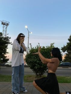 a woman kneeling down next to a man on the sidewalk with his hand up in front of her face