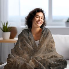 a smiling woman wrapped in a blanket sitting on a couch