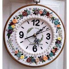 a white clock with flowers on it hanging from the side of a door