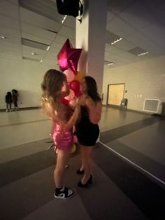 two young women are hugging each other in an empty room with pink and yellow balloons