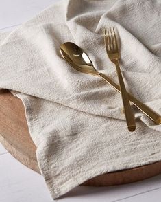 two gold forks and spoons on a white linen napkin next to a wooden bowl