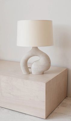 a white table lamp sitting on top of a wooden block with a beige shade over it