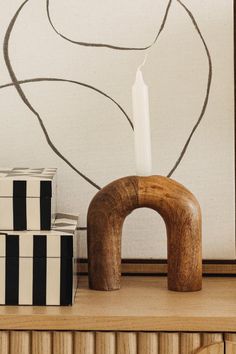 a white candle sitting on top of a wooden table next to boxes and a painting