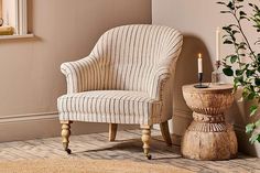 a striped chair next to a wooden table with a candle on it