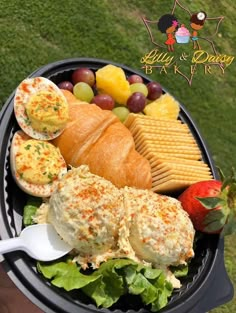 a plate with bread, cheese, fruit and crackers in it on the grass