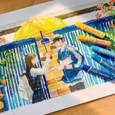 some crayons are laying on top of a piece of paper with an image of two people holding umbrellas