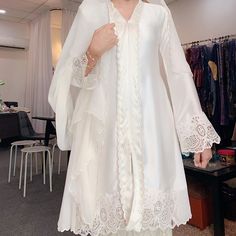 a woman wearing a white robe and hat standing in front of a rack of clothes