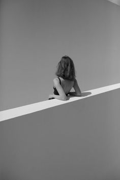 a woman sitting on top of a white ledge next to a wall with her head down