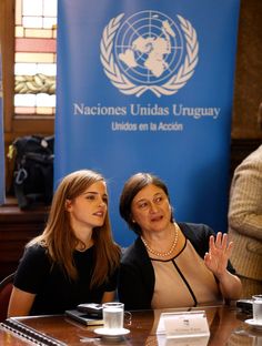 two women sitting at a table in front of a blue sign with the logo of the un