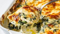 a casserole dish with spinach and cheese being lifted from the casserole