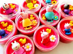 many plastic toy animals are in small pink containers with flowers on the bottom and one pig sitting on top