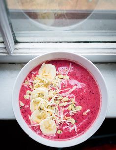 a white bowl filled with red smoothie and banana slices next to a window sill