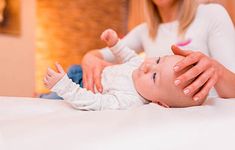 a woman holding a baby on top of a bed with her hands in the air