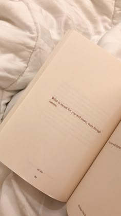 an open book sitting on top of a bed next to a white comforter and pillows