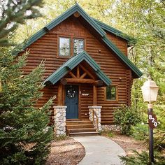 a log cabin with a blue door and green roof is surrounded by greenery, trees and shrubs