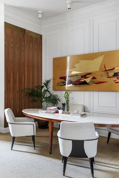 a dining room table with two chairs and a large painting on the wall behind it