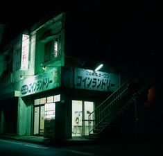 a dark street at night with a lit up store front and stairs leading to it