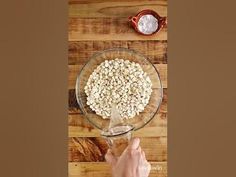 someone is mixing ingredients in a bowl on a wooden table with a measuring cup and spoon