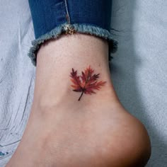 a small leaf tattoo on the ankle that is red and orange with green leaves around it