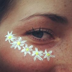 a woman's eye with white flowers painted on her cheek and eyeshade